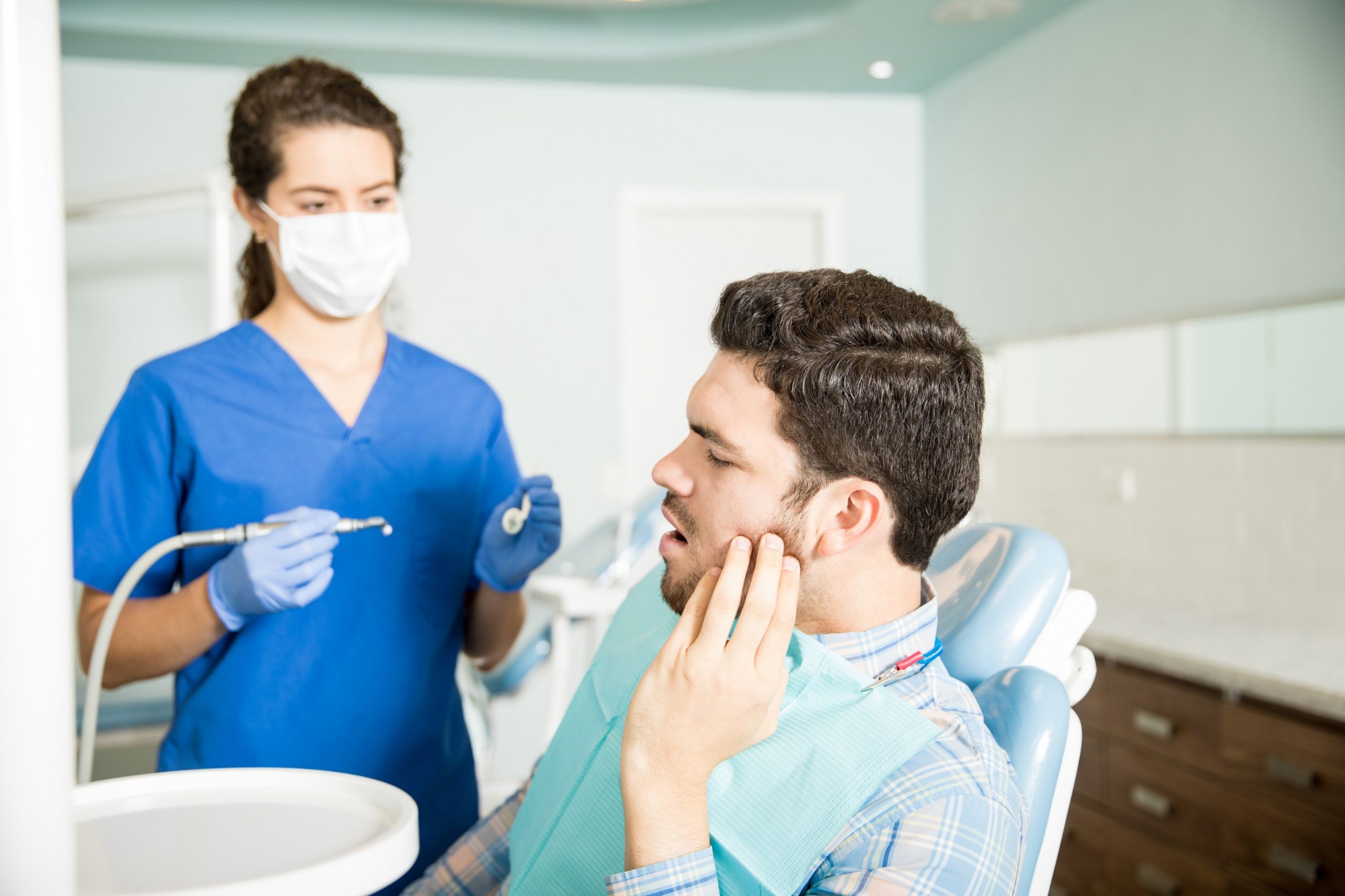 Mid adult man suffering from toothache while looking dentist with tools clinic (1)