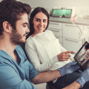 Beautiful woman and handsome dentist are studying image of patient's teeth on a digital tablet